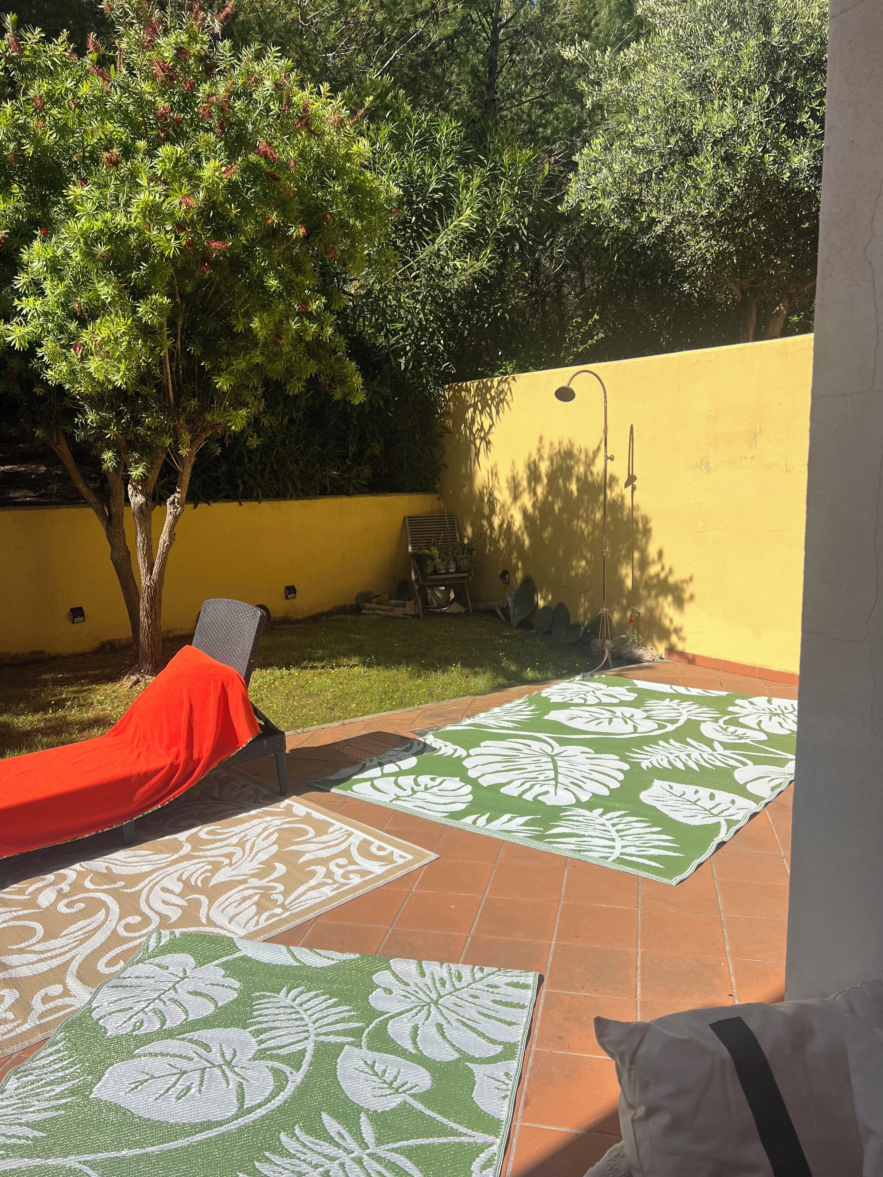 A patio with a red lounge chair, a patterned mat, and a tree.