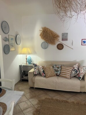 Una sala de estar con un sofá color beige, cojines decorativos, un tapete tejido, obras de arte en la pared y una lámpara.