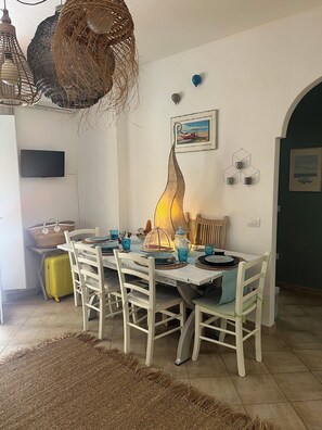 A dining area with a table set for four, white chairs, a woven hanging light fixture, and a wall-mounted picture. - House with a garden in Santa Teresa di Gallura (Santa Teresa di Gallura)