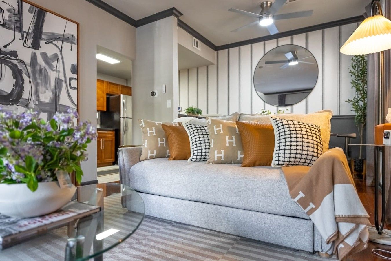 A modern living room with a sofa, decorative pillows, a glass coffee table, and a large mirror on the wall.