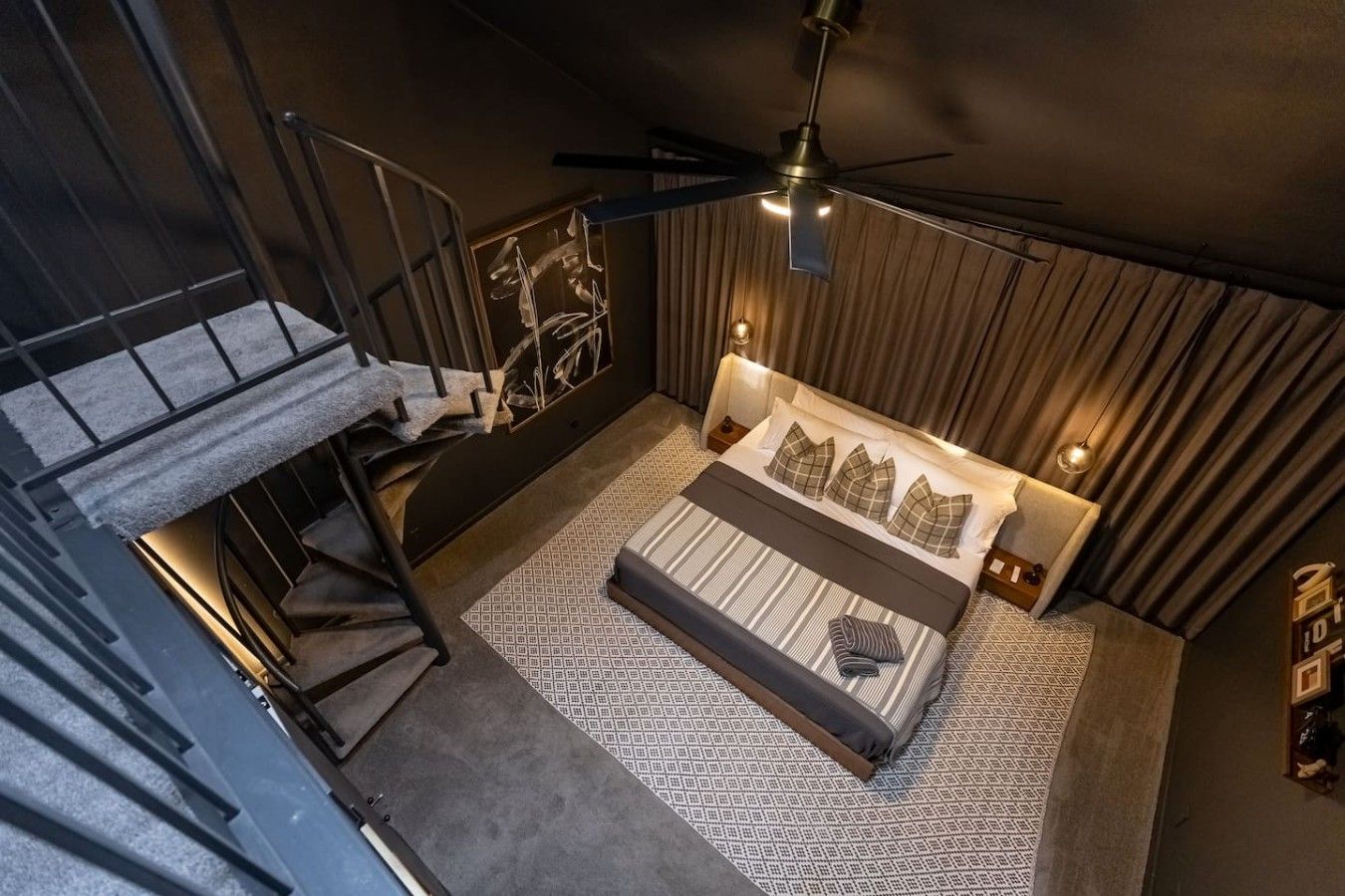 A bedroom with a bed, a ceiling fan, and a staircase.