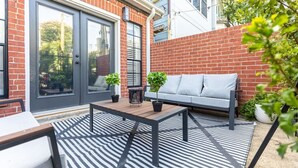 Eine Terrasse mit Sofa, Tisch und Stühlen, einer Tür und einer Backsteinmauer.