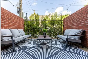 An outdoor seating area with two sofas and a table, surrounded by a brick wall and a metal fence. - Montrose Luxury Stay | Prime Location + Patio (Houston)