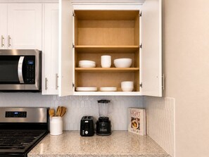Una cocina con gabinetes blancos, un microondas, un tostador, una licuadora y un libro de cocina sobre la encimera.