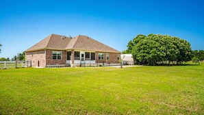 A single-story brick building with a flat roof, a covered porch, and a large tree in the foreground. - Family Country Home | Gaming, Workspace, Yard (Terrell)