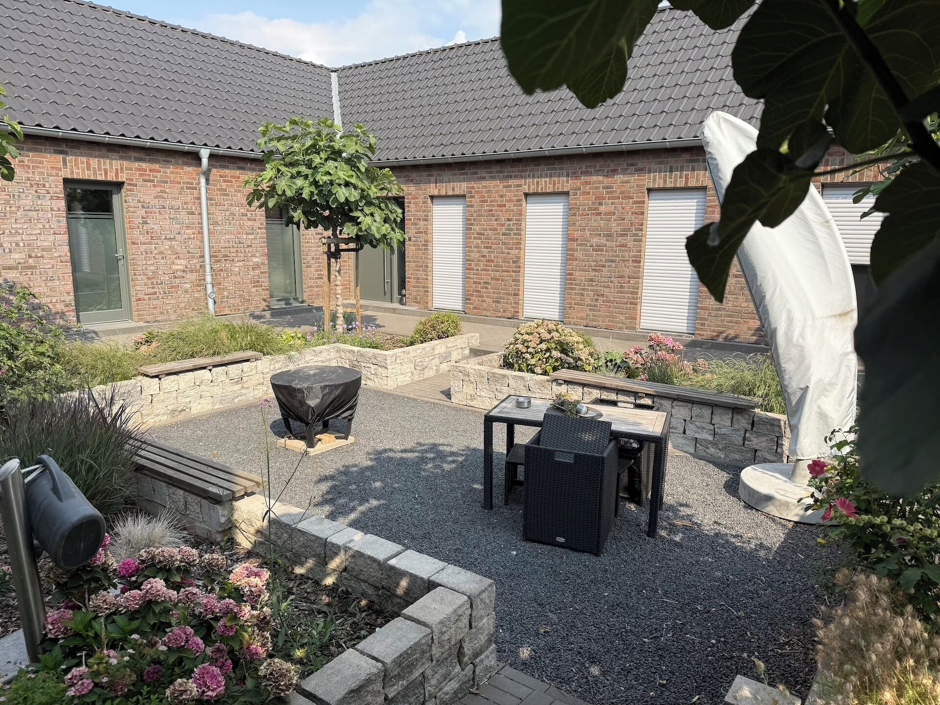 A courtyard with a barbecue grill, outdoor seating, and a brick building with garage doors.