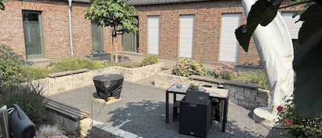 A courtyard with a barbecue grill, outdoor seating, and a brick building with garage doors.