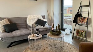 A modern living room with a grey sofa, two small round tables, a coffee table with decorative items, and a bookshelf with books and a ladder. - Lindenglück Vacation Rental (Uedem)