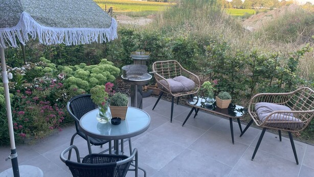 An outdoor patio with wicker furniture, a round table, and a decorative umbrella. - Lindenglück Vacation Rental (Uedem)