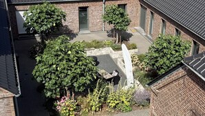 A courtyard with brick buildings, a paved area, and various plants. - Lindenglück Vacation Rental (Uedem)