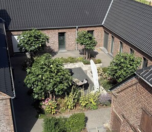 A courtyard with brick buildings, a paved area, and various plants. - Lindenglück Vacation Rental (Uedem)