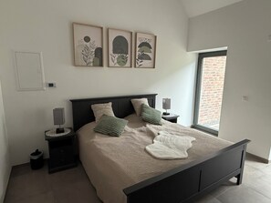 Ein Schlafzimmer mit einem Bett, zwei Nachttischen, einem Fenster und drei gerahmten Kunstwerken an der Wand.