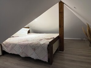 A bedroom with a sloped ceiling, a bed with a quilt, a bedside lamp, and a wooden floor. - Lindenglück Vacation Rental (Uedem)