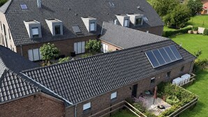A residential building with multiple skylights and solar panels on the roof, surrounded by a well-maintained lawn and garden. - Lindenglück Vacation Rental (Uedem)