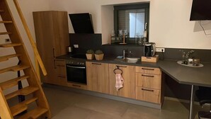 A modern kitchen with wooden cabinets, a built-in oven, a sink, and a window above the counter. - Lindenglück Vacation Rental (Uedem)
