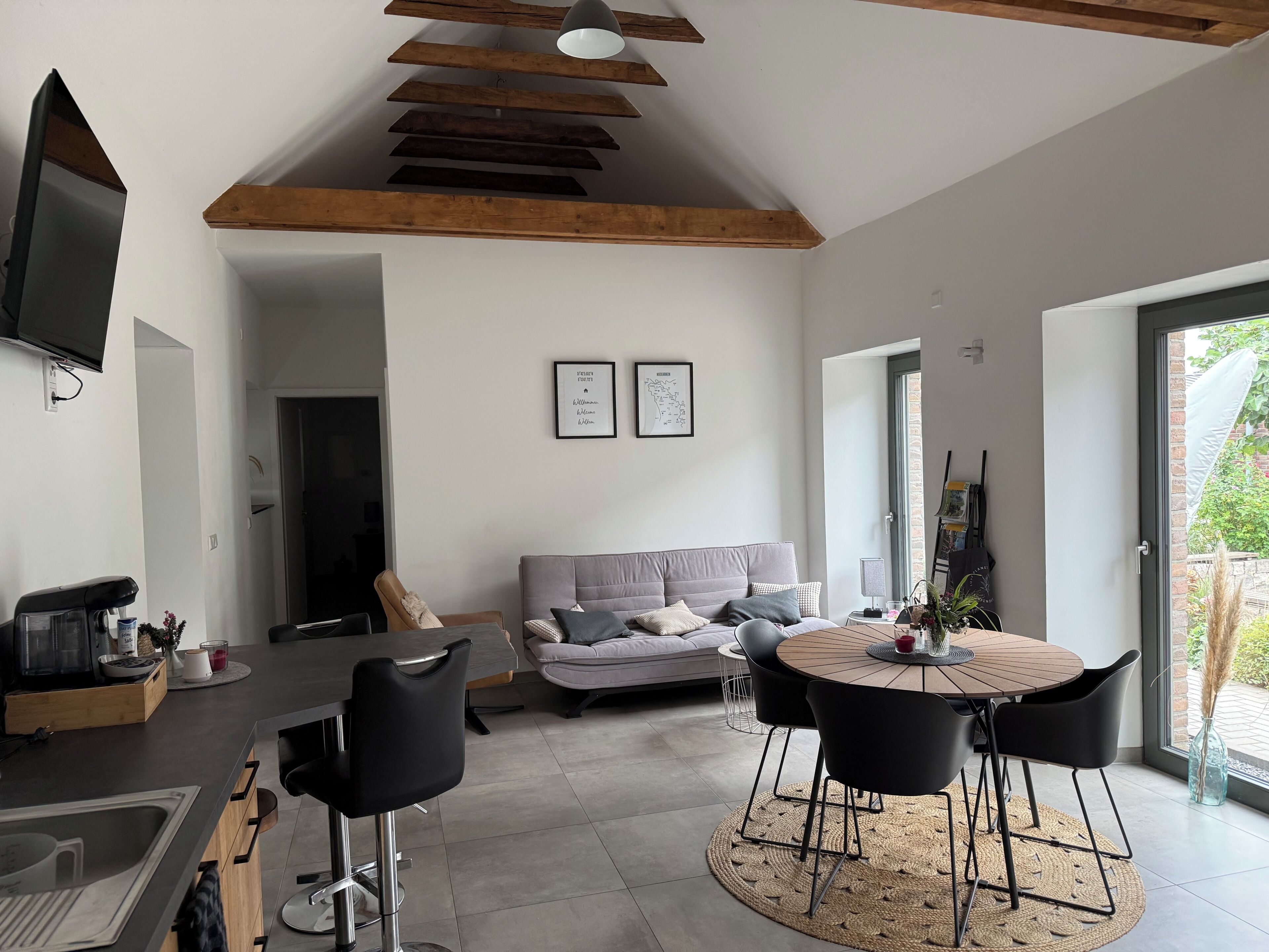 A modern living space with a kitchen area, a dining table with chairs, a sofa, and a television mounted on the wall.