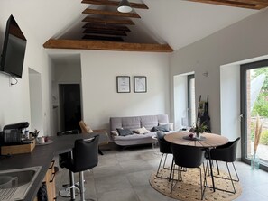 Ein modernes Wohnzimmer mit Küchenzeile, einem Esstisch mit Stühlen, einer Couch und einem an der Wand befestigten Fernseher.