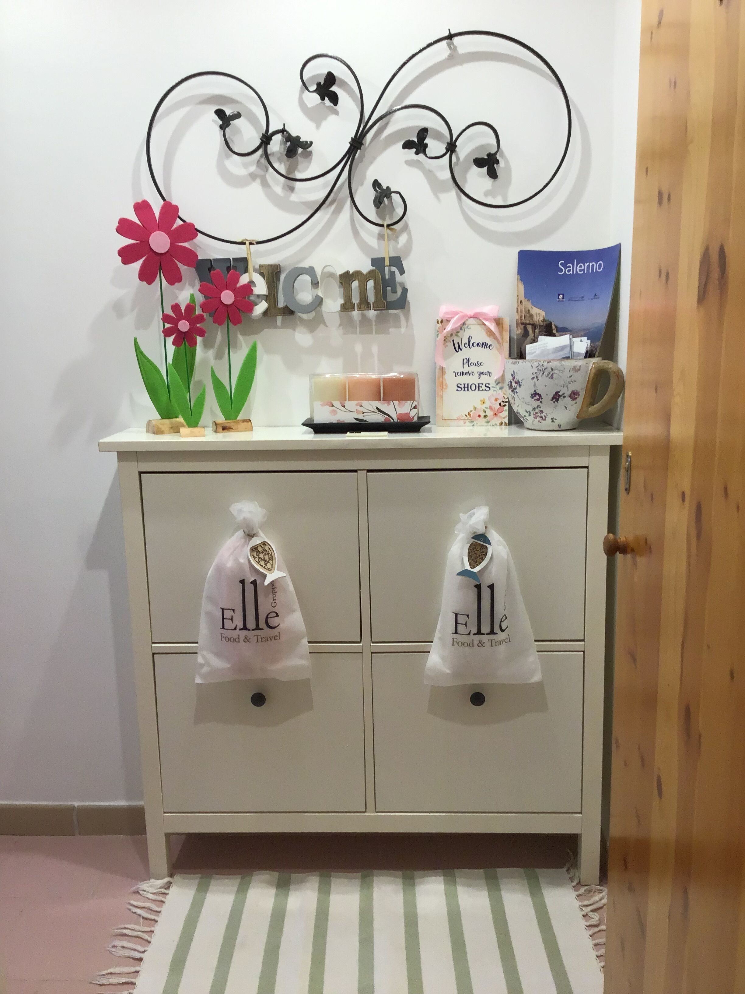 Un armadietto bianco con un cartello decorativo in metallo, un segnale di benvenuto, una locandina da viaggio e due borse appese alle ante.