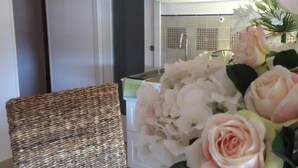 Una silla de mimbre y un arreglo floral en una habitación con un armario blanco y salpicadero de azulejos.