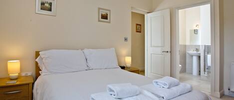 Une chambre d’hôtel comprenant un lit, deux tables de chevet, une commode, une salle de bain avec un lavabo et un miroir, et deux tableaux encadrés accrochés au mur.