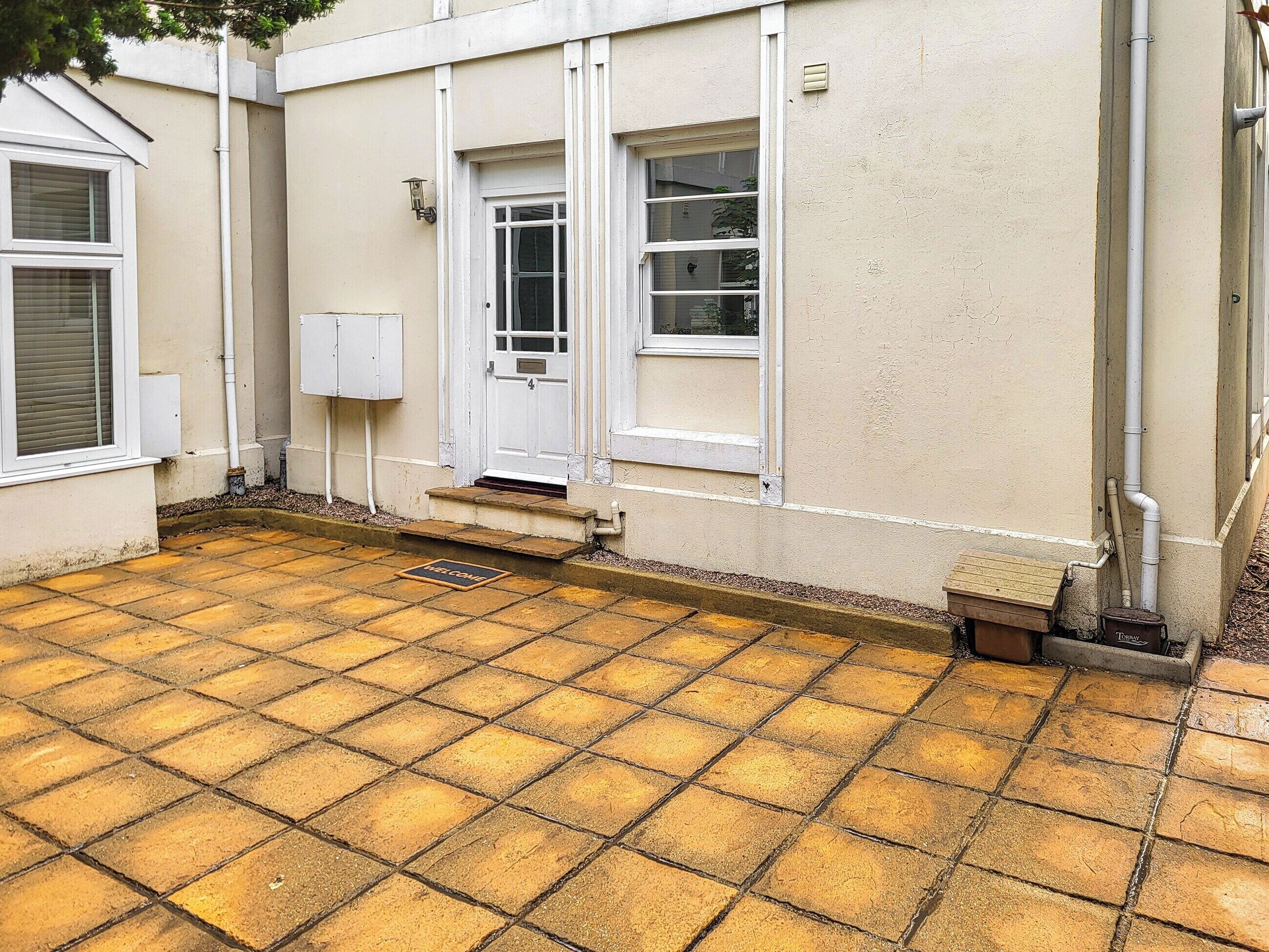 Een gebouw met een betegeld terras, een witte deur en een brievenbus.
