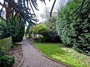 A gravel pathway leading through a garden with dense foliage and a wooden fence on one side. - A modern well-appointed apartment in a convenient location. (Torquay)