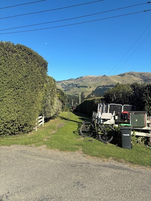 A gravel path leading to a vehicle parked beside a hedge, with a mountain range in the background.