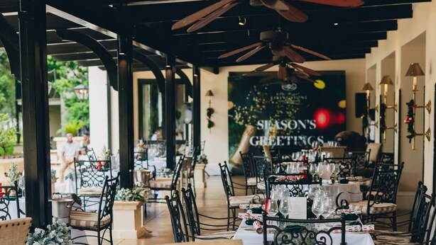 Un espace de restauration en plein air avec des tables dressées pour un repas, comprenant des chaises en métal et un ventilateur de plafond.