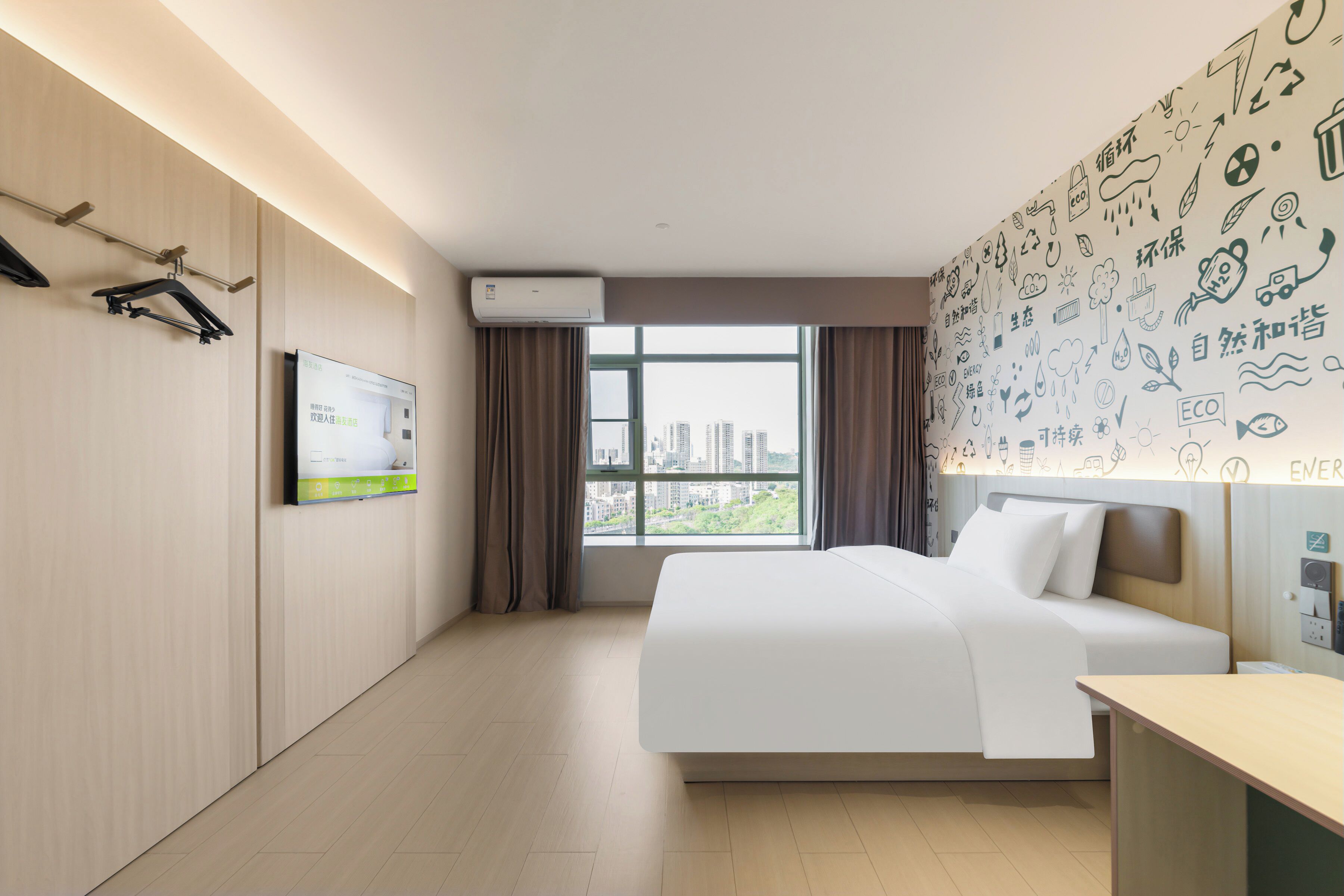 Una camera d'hotel con un letto, una scrivania, una TV a parete e una finestra con vista sulla città.