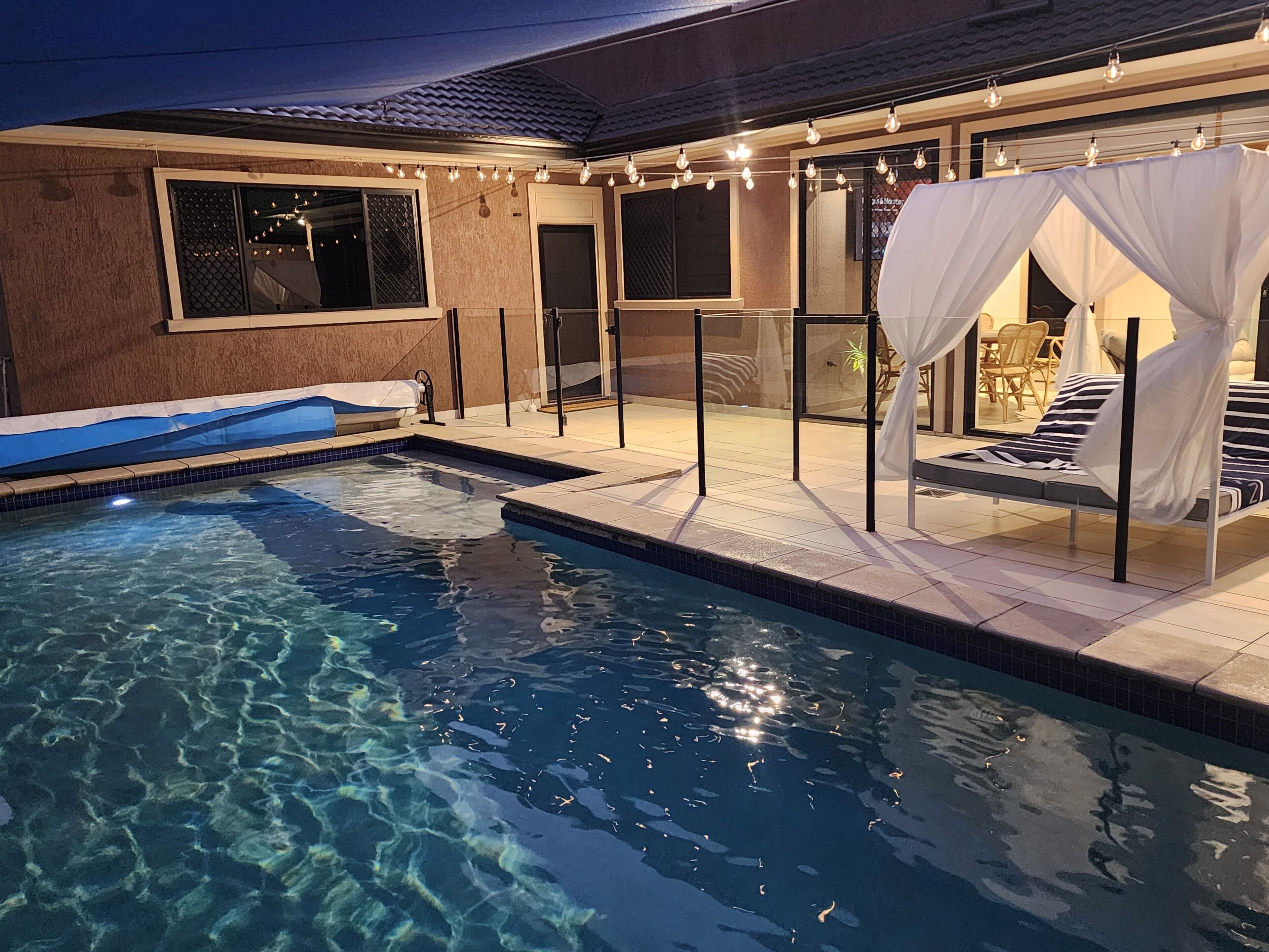 Une piscine à l’eau claire, un espace détente couvert avec un auvent, et une terrasse avec des meubles d’extérieur.