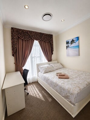 Een slaapkamer met een bed, een bureau en een schilderij van een strandgezicht.