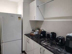 A kitchen with white cabinets, a black countertop, and various appliances including a refrigerator, coffee maker, and toaster.