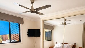 A hotel room with two beds, a television, a ceiling fan, and a dining area with a table and chairs.