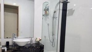 A modern bathroom with a glass-enclosed shower, a white sink, and a marble countertop.