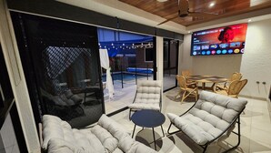 A modern lounge area with a glass partition, cushioned seating, a small round table, and a flat-screen TV mounted on the wall.