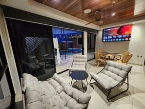 A modern lounge area with a glass partition, cushioned seating, a small round table, and a flat-screen TV mounted on the wall.