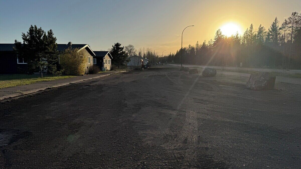 Une rue résidentielle bordée de maisons, un ciel dégagé et le soleil se couchant ou se levant.