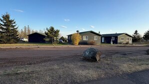 Una zona residencial con dos casas, un camino de tierra y una roca grande al frente.
