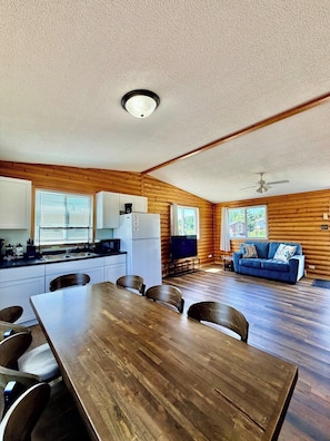 A cabin interior with a dining table, chairs, a kitchenette, a sofa, and a ceiling fan. - 1818 Trailside Birch - Cabin 1 (Grand Marais)