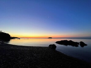 En strandscene med roligt vand, småsten og klipper.