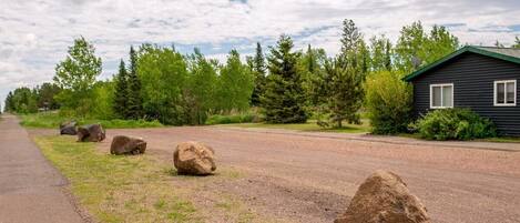 A rural road with large rocks, a gravel path, and a cabin with a green roof.
