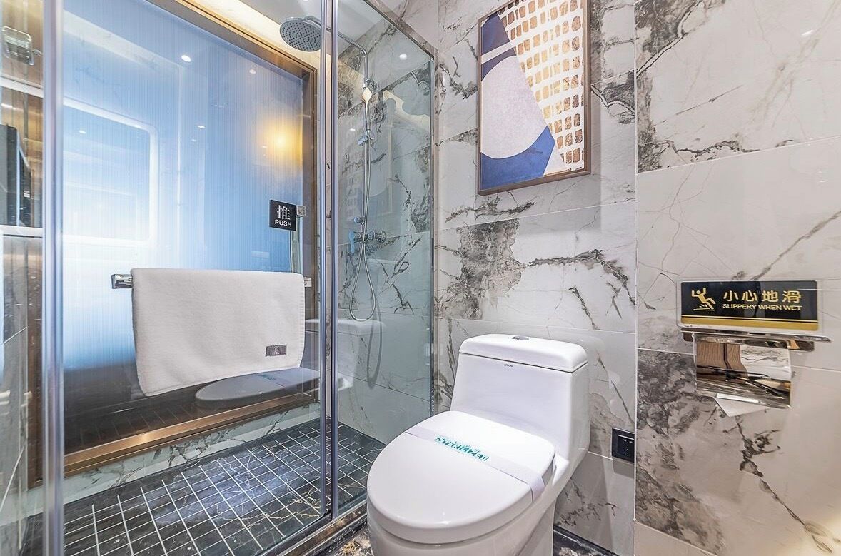 A modern bathroom with a glass shower enclosure, a white toilet, and a marble wall.