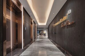 A hotel corridor with a modern design, featuring a marble floor and a wall-mounted sign.