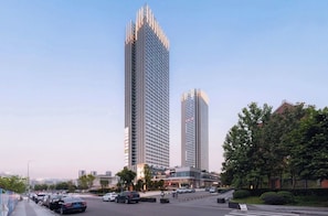 A modern high-rise building with a glass facade, surrounded by a street with parked cars and a pedestrian crossing.