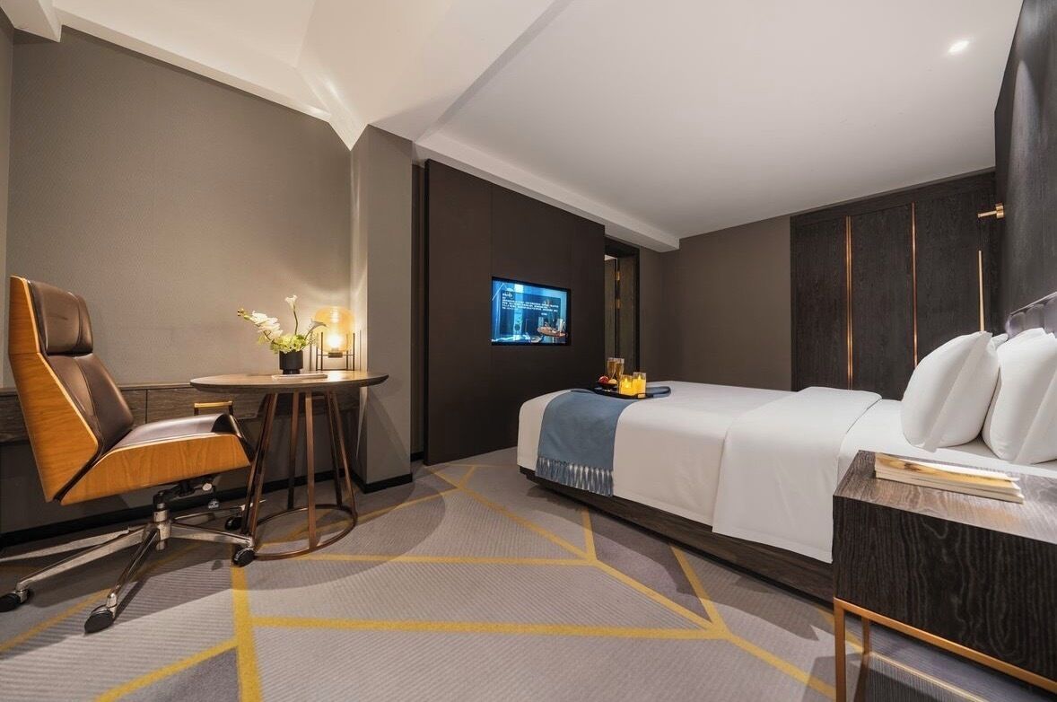 Habitación de hotel con cama, escritorio y silla, televisión y una pequeña mesa con un florero.