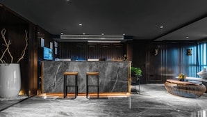 Eine moderne Lobby mit einem Marmor-Empfangsschalter, zwei Barhocker, einem Korbtisch und einer Couch.