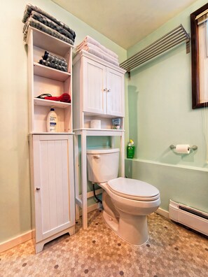 Een badkamer met een toilet, een kast met handdoeken en een douchehoek.