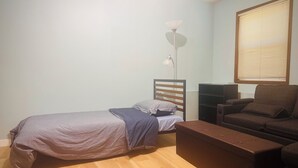 Un dormitorio con cama, escritorio, silla, lámpara de pie y ventana con persianas.