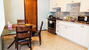 A kitchen with white cabinets, a microwave, and a stove. There is a dining table with chairs and a small fruit bowl.
