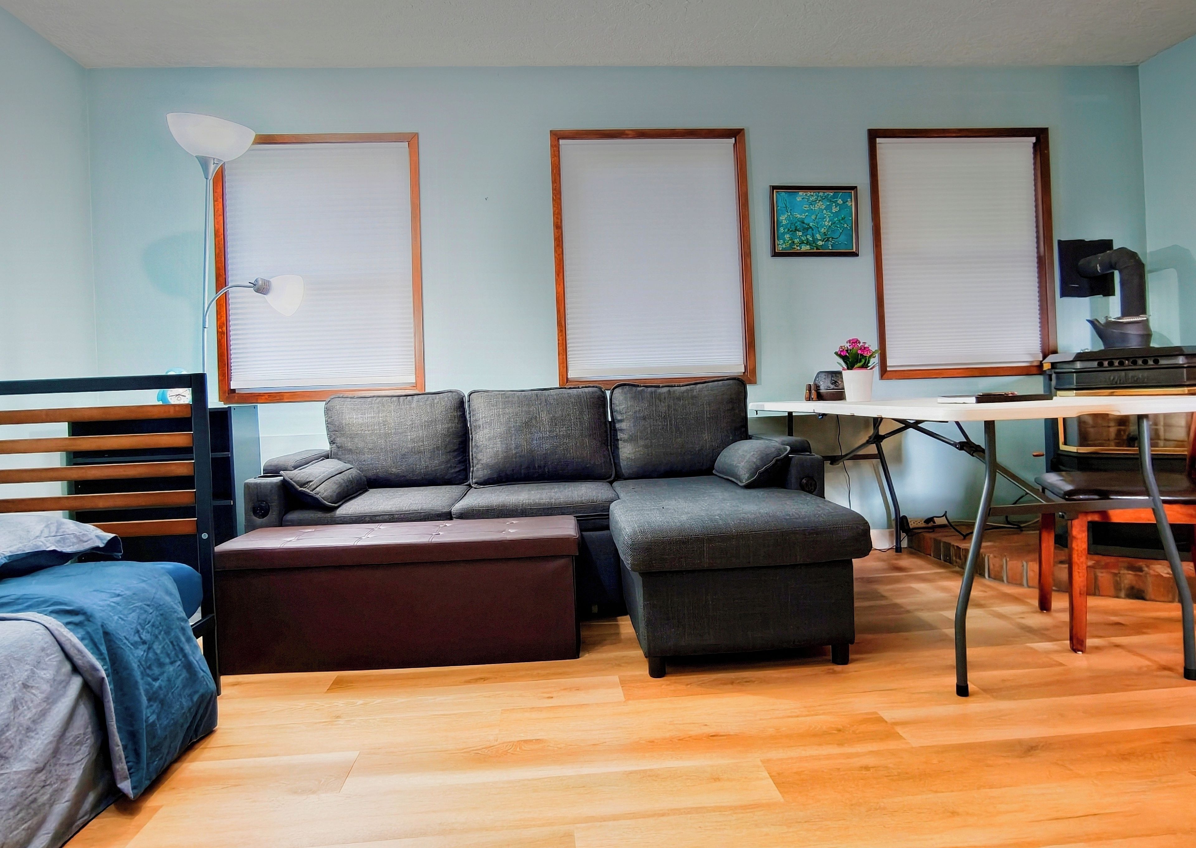 Un espace de vie compact comprenant un canapé, un pouf et un bureau avec une bouilloire.